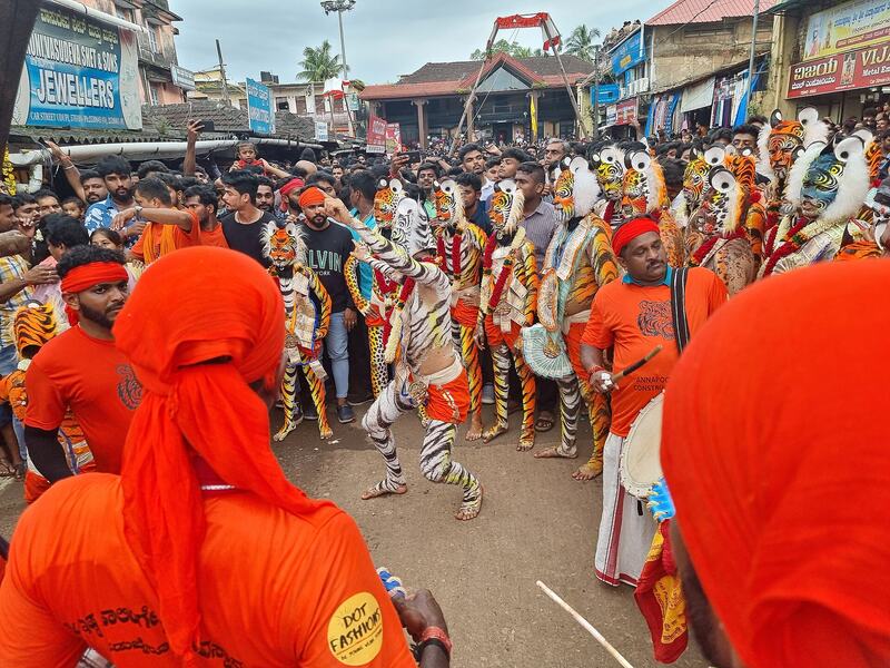 Dancers painted as tigers perform in a crowded street with a drummer beside them.
